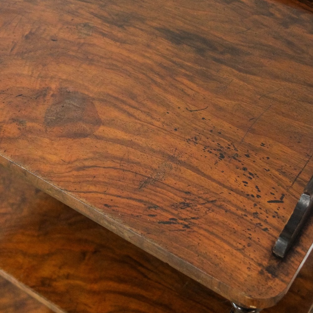 A three-tiered Victorian walnut whatnot stand featuring turned support columns, a single base drawer with turned wooden knobs, and brass castors. View VI