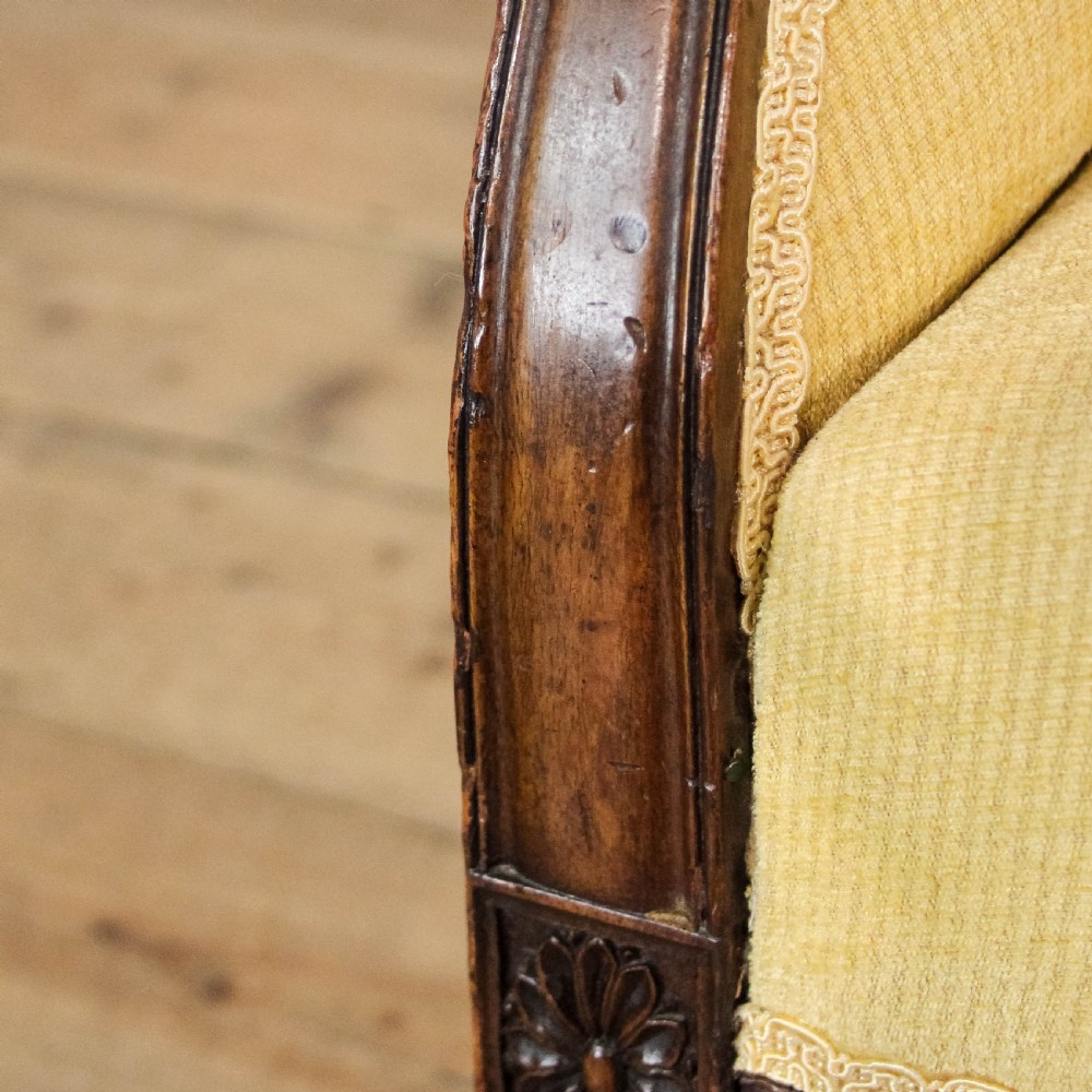An Edwardian armchair with pale yellow fabric upholstery, a dark mahogany frame with sweeping armrests, square tapered front legs, and brass castors. View VIII