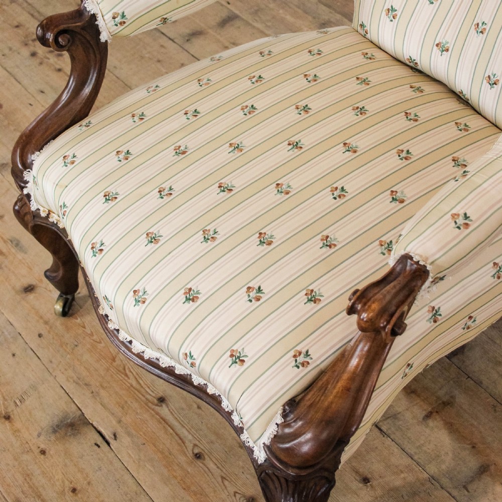 An antique Victorian armchair featuring dark carved wood legs with brass castors and cream-and-green striped floral fabric upholstery with a buttoned backrest. View VIII