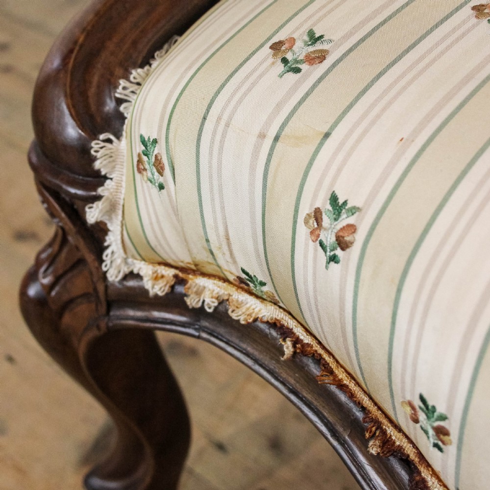 An antique Victorian armchair featuring dark carved wood legs with brass castors and cream-and-green striped floral fabric upholstery with a buttoned backrest. View IX