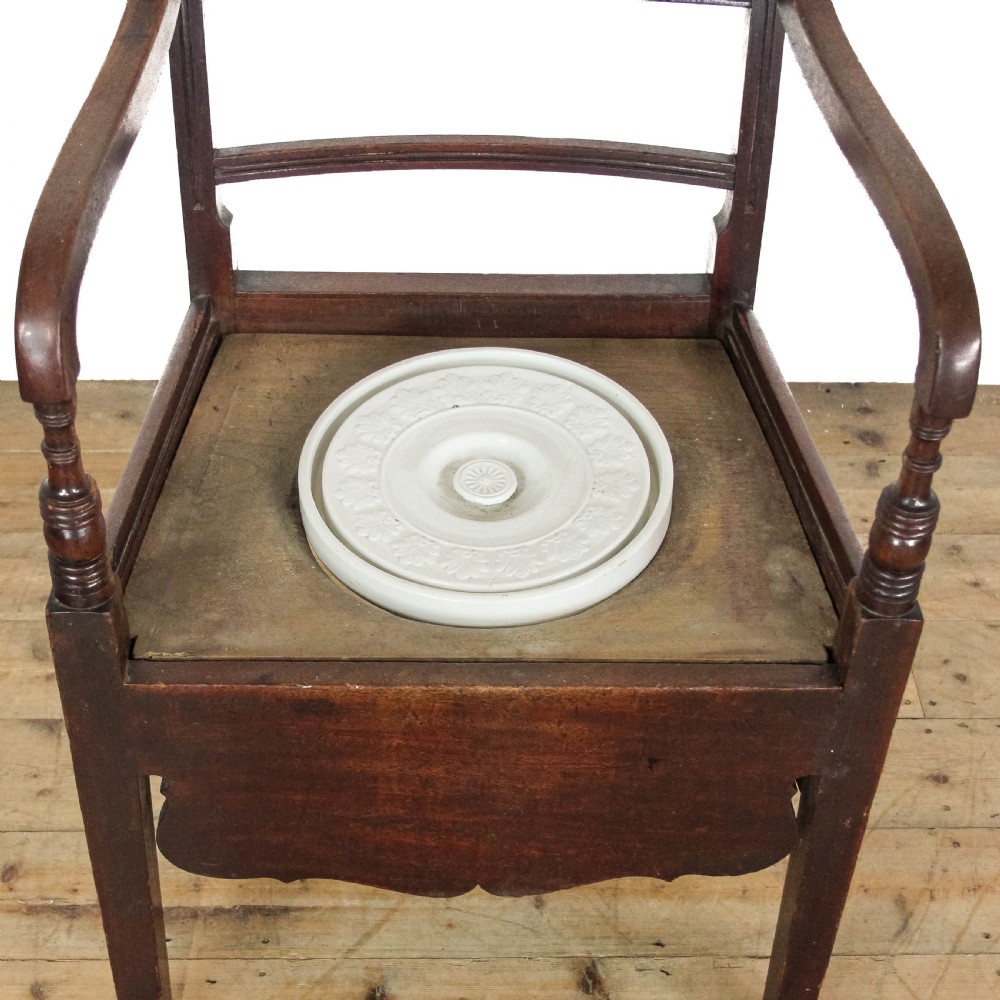 An antique dark mahogany commode chair featuring turned arm supports, a bar back frame, and an olive green drop-in seat pad. View X