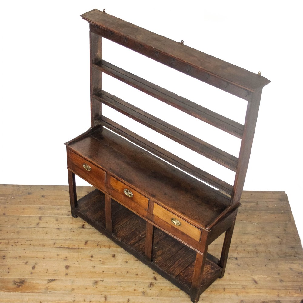 An antique dark oak open-potboard dresser featuring an upper three-tier plate rack with hooks, three drawer units with brass oval handles, and four square legs supporting a slatted lower shelf. View II