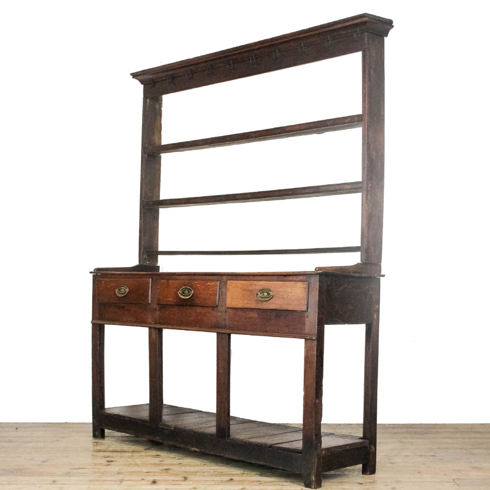 An antique dark oak open-potboard dresser featuring an upper three-tier plate rack with hooks, three drawer units with brass oval handles, and four square legs supporting a slatted lower shelf. View III
