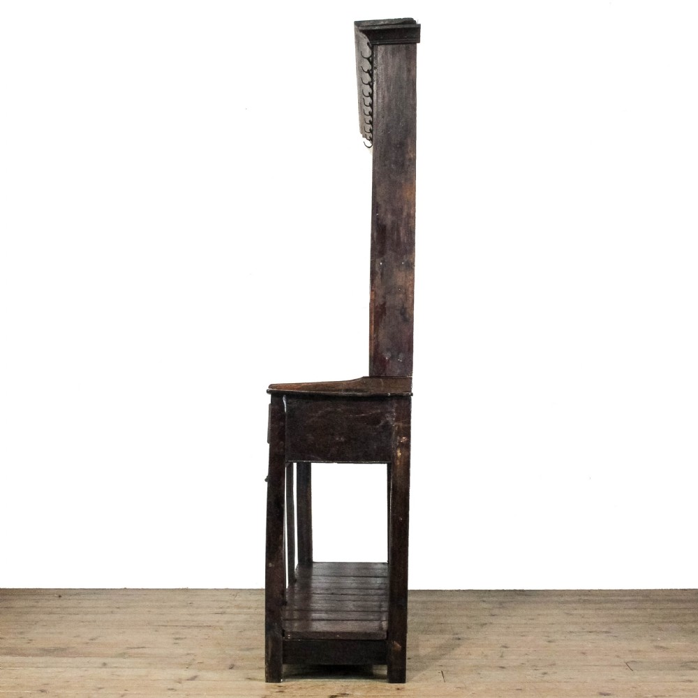 An antique dark oak open-potboard dresser featuring an upper three-tier plate rack with hooks, three drawer units with brass oval handles, and four square legs supporting a slatted lower shelf. View VI