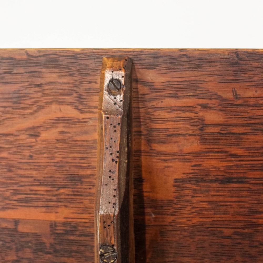 An antique oak square tripod table displaying its tilt-top position vertically above a turned central column and three curved legs. View III