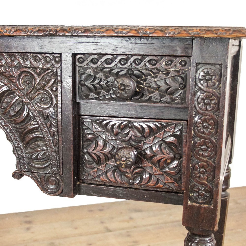 A dark-stained antique oak side table featuring intricate foliate relief carvings, a central arched kneehole, four small drawers, and turned legs. View VIII