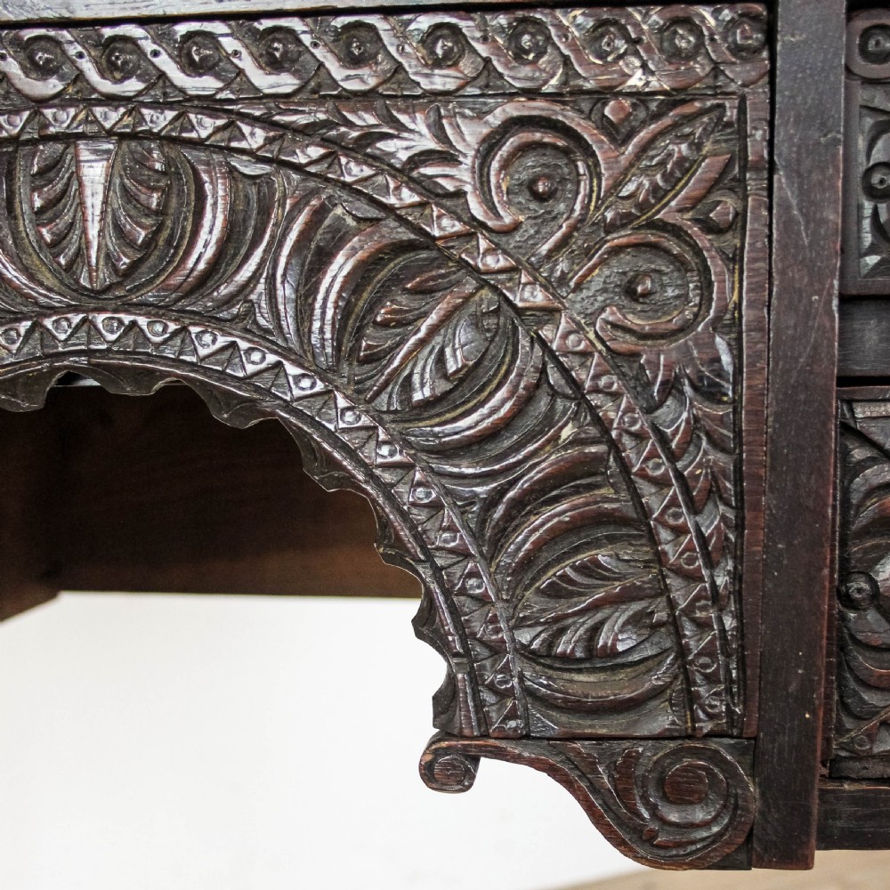A dark-stained antique oak side table featuring intricate foliate relief carvings, a central arched kneehole, four small drawers, and turned legs. View IX