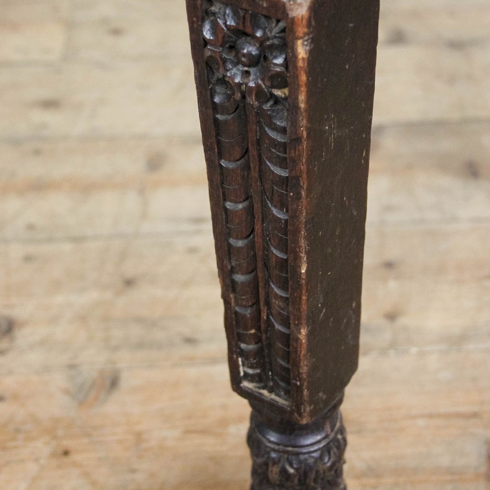 A dark-stained antique oak side table featuring intricate foliate relief carvings, a central arched kneehole, four small drawers, and turned legs. View X