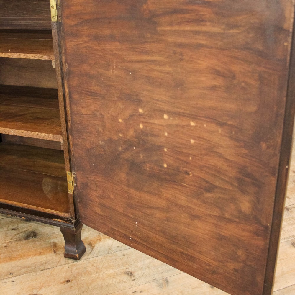 An early 20th-century dark oak music cabinet featuring a slanted top surface, carved trim, a single panelled door, and short carved legs. View VI