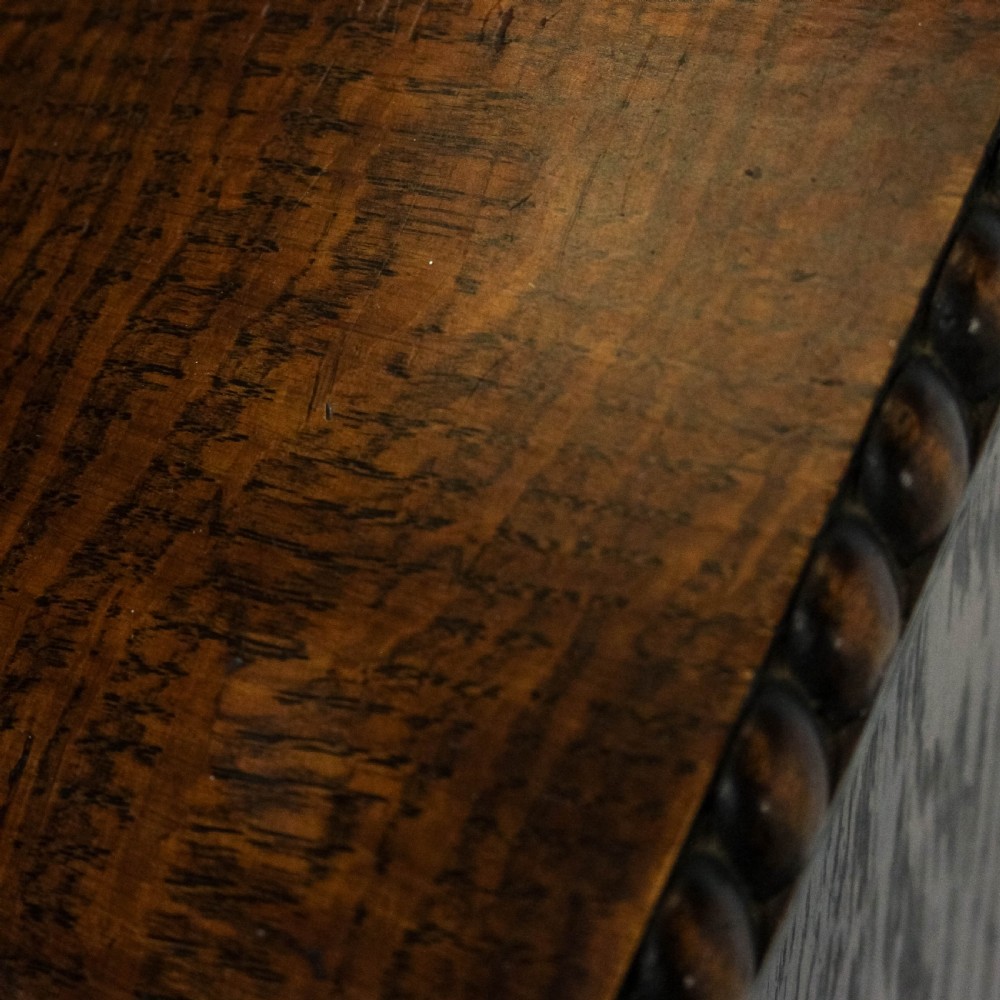 An early 20th-century dark oak music cabinet featuring a slanted top surface, carved trim, a single panelled door, and short carved legs. View XI