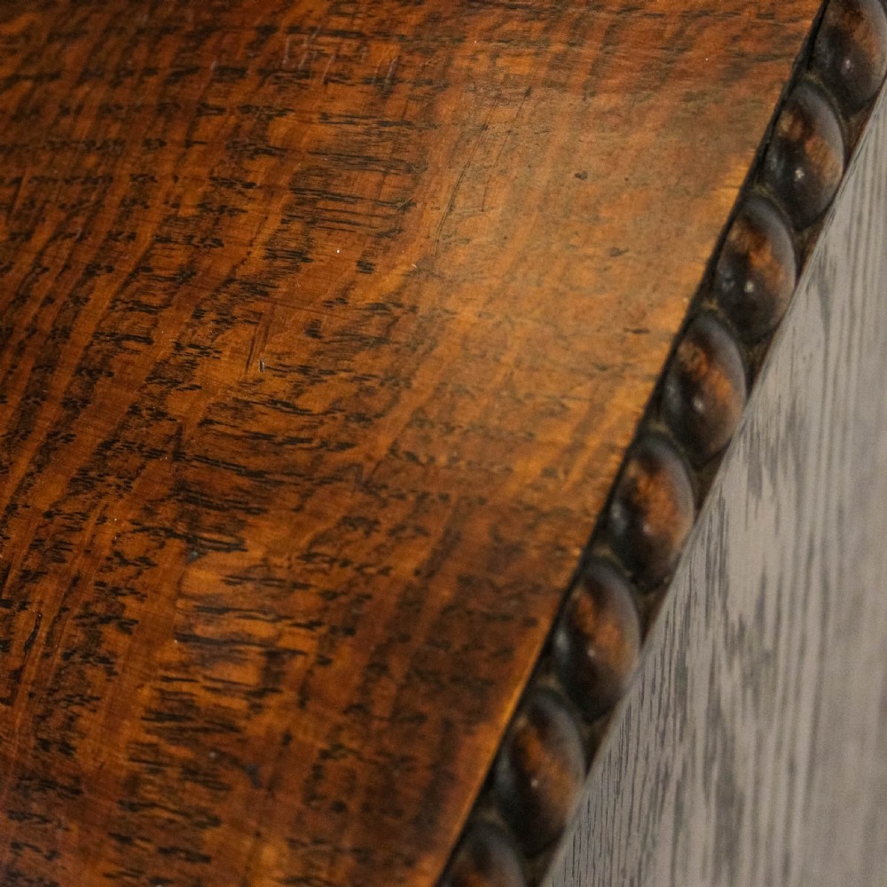 An early 20th-century dark oak music cabinet featuring a slanted top surface, carved trim, a single panelled door, and short carved legs. View XII