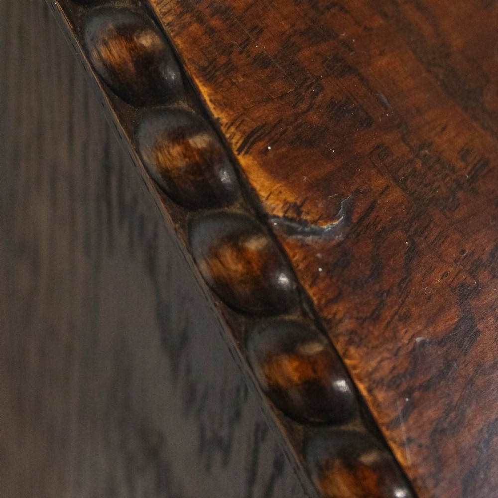 An early 20th-century dark oak music cabinet featuring a slanted top surface, carved trim, a single panelled door, and short carved legs. View XIII
