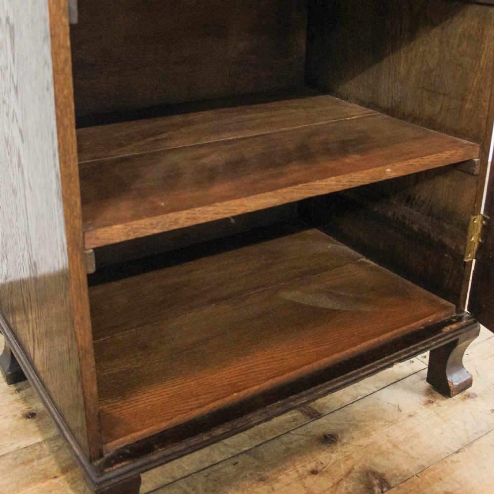 An early 20th-century dark oak music cabinet featuring a slanted top surface, carved trim, a single panelled door, and short carved legs. View XIV