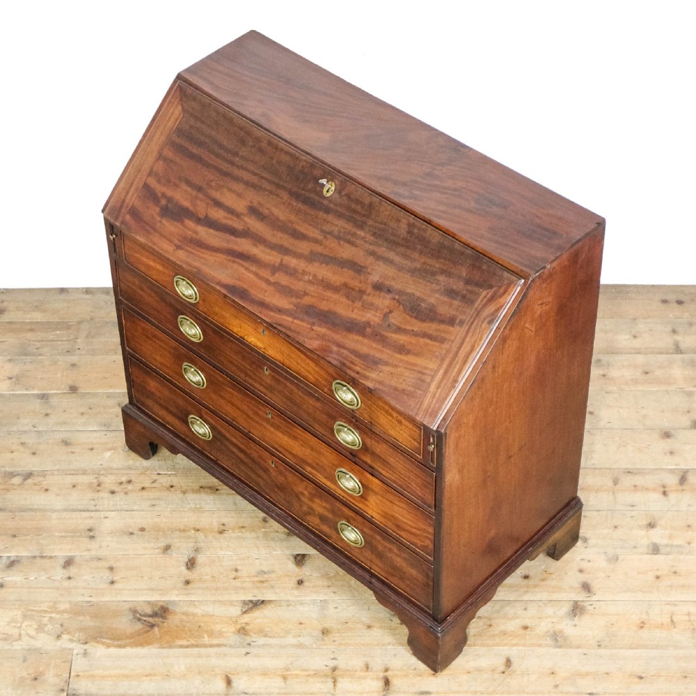 An antique mahogany writing bureau with a slant-front fall, four graduated drawers, oval brass handles, and bracket feet. View III