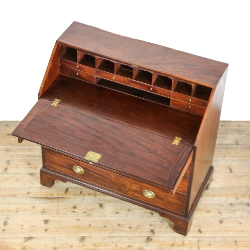 An antique mahogany writing bureau with a slant-front fall, four graduated drawers, oval brass handles, and bracket feet. View XV