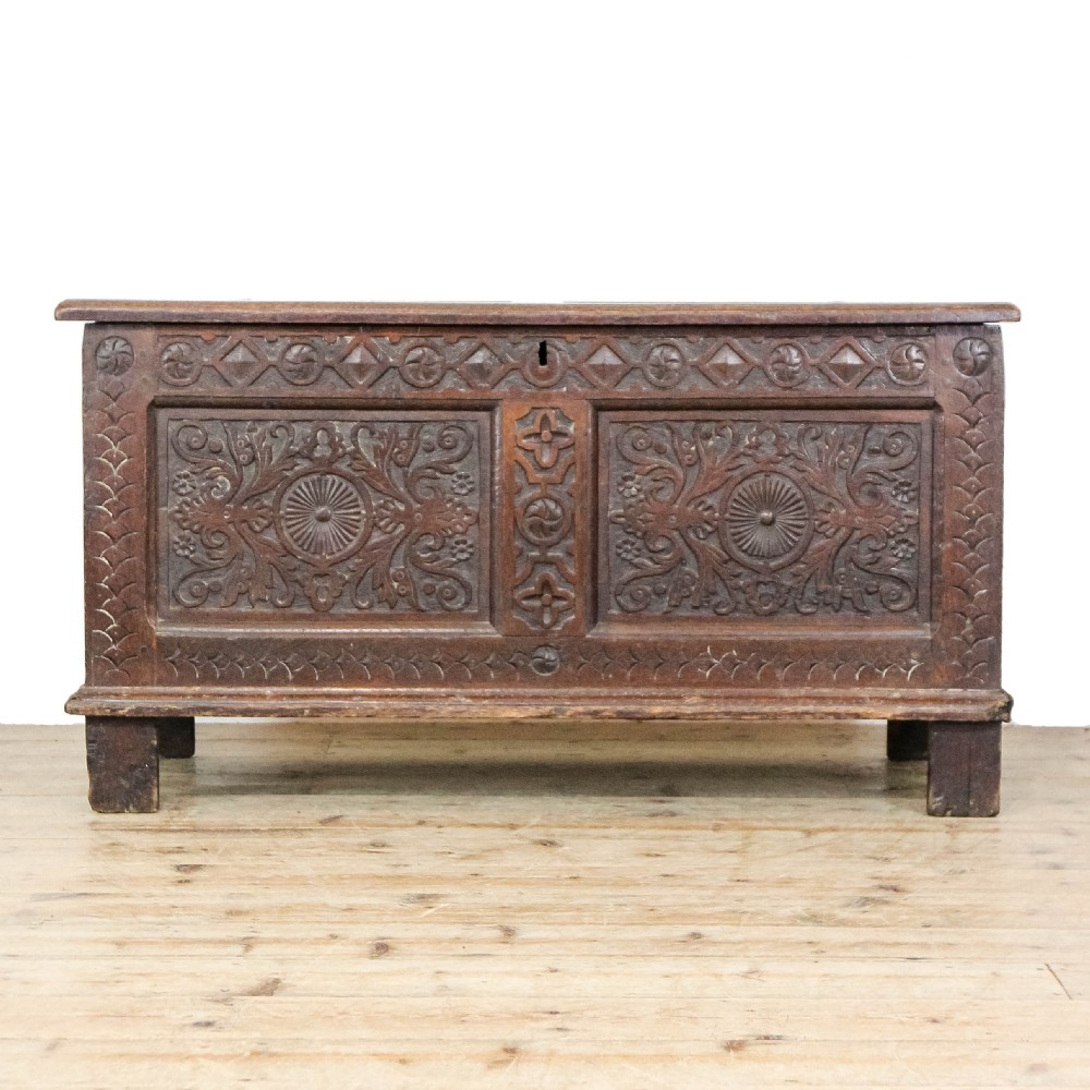 A 19th-century dark oak coffer featuring carved floral scroll panels, a decorative frieze, and sturdy block feet.