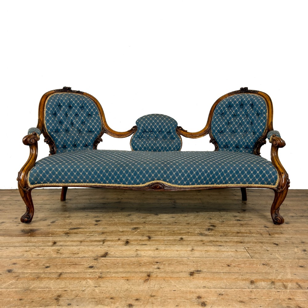 A Victorian carved walnut settee with double button-tufted balloon backrests and blue patterned fabric upholstery.