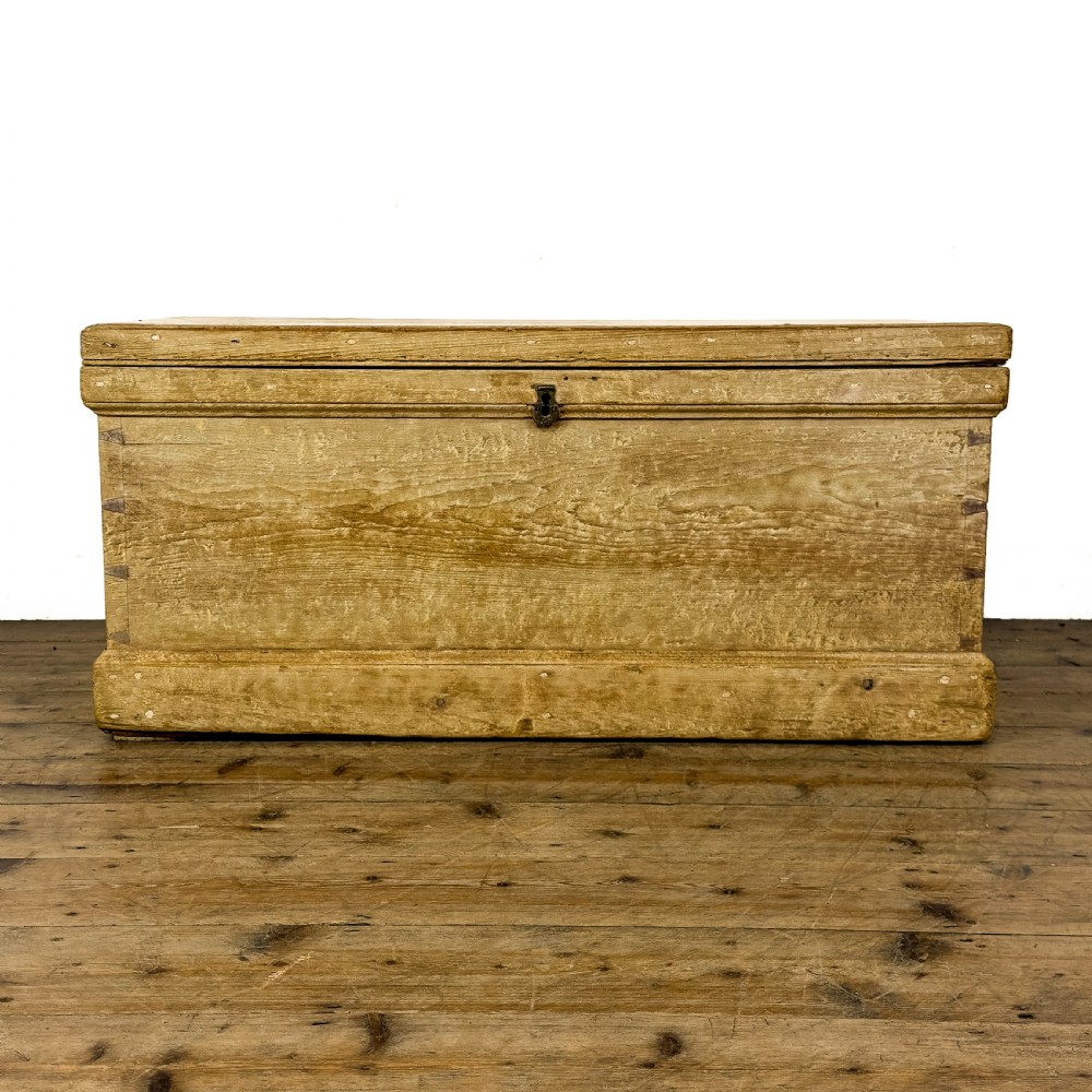 A rectangular natural pine blanket box featuring hand-cut dovetail joints, a hinged top lid, a moulded plinth base, and a central metal escutcheon.