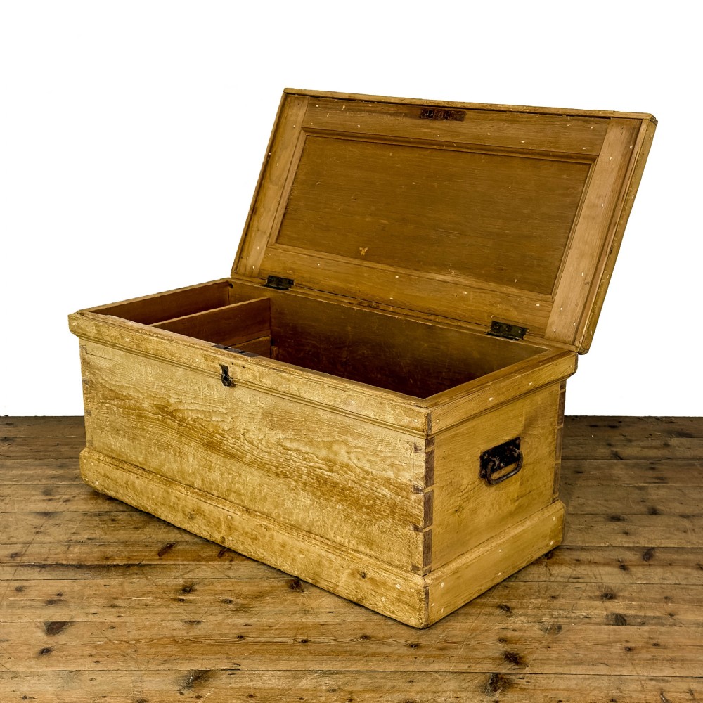 A rectangular natural pine blanket box featuring hand-cut dovetail joints, a hinged top lid, a moulded plinth base, and a central metal escutcheon. View V