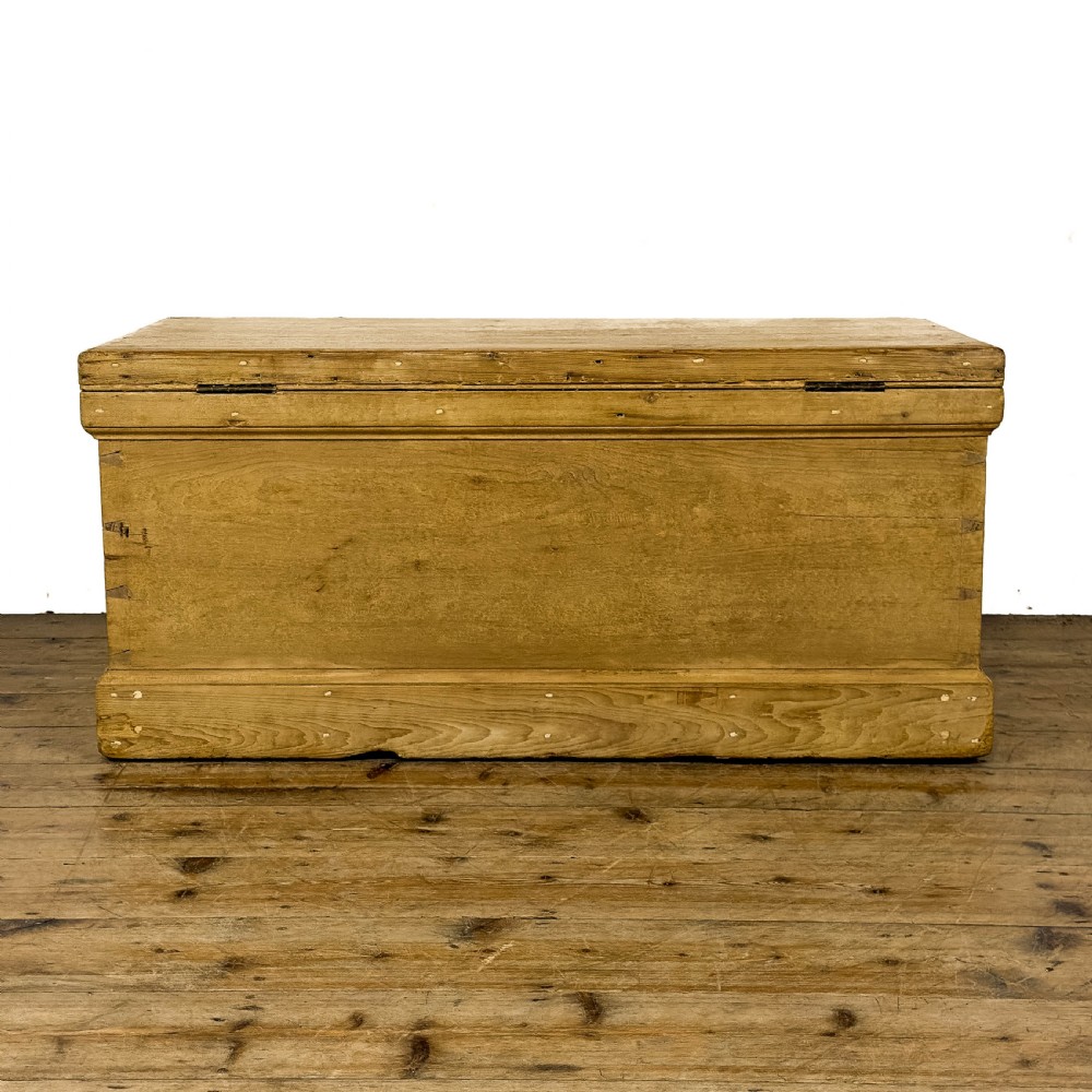 A rectangular natural pine blanket box featuring hand-cut dovetail joints, a hinged top lid, a moulded plinth base, and a central metal escutcheon. View VII