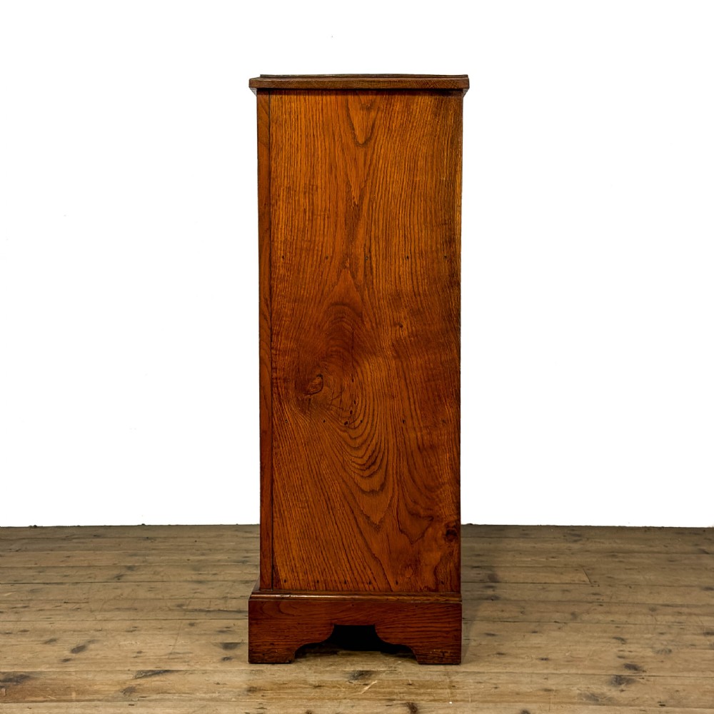 An antique warm brown oak cupboard featuring two moulded panel doors, polished brass escutcheons, and a shaped plinth base. View IV