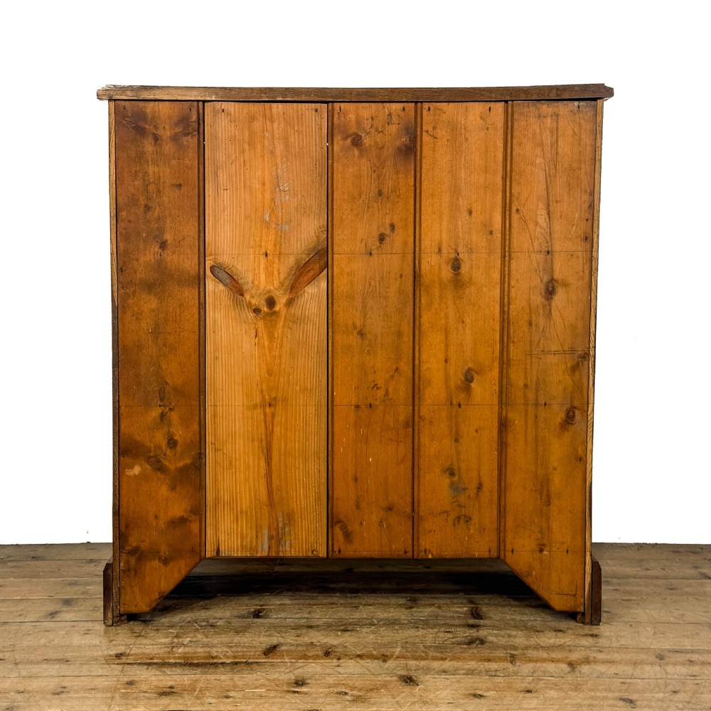 An antique warm brown oak cupboard featuring two moulded panel doors, polished brass escutcheons, and a shaped plinth base. View V