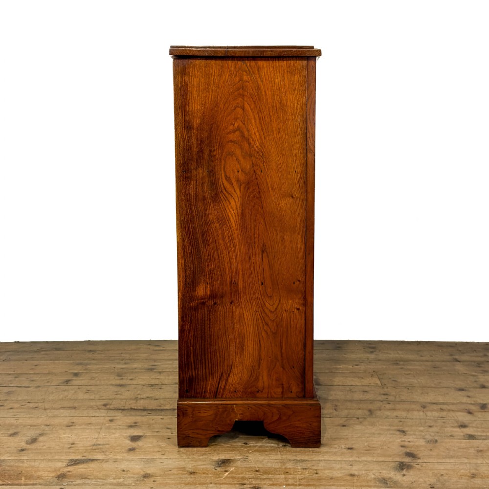 An antique warm brown oak cupboard featuring two moulded panel doors, polished brass escutcheons, and a shaped plinth base. View VI