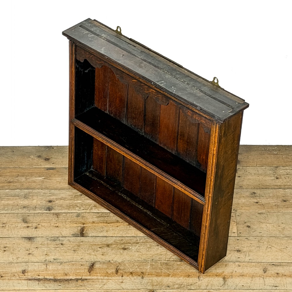 A dark brown oak two-tier wall-hanging shelf unit featuring a scalloped top frieze and vertical planked backboard. View III