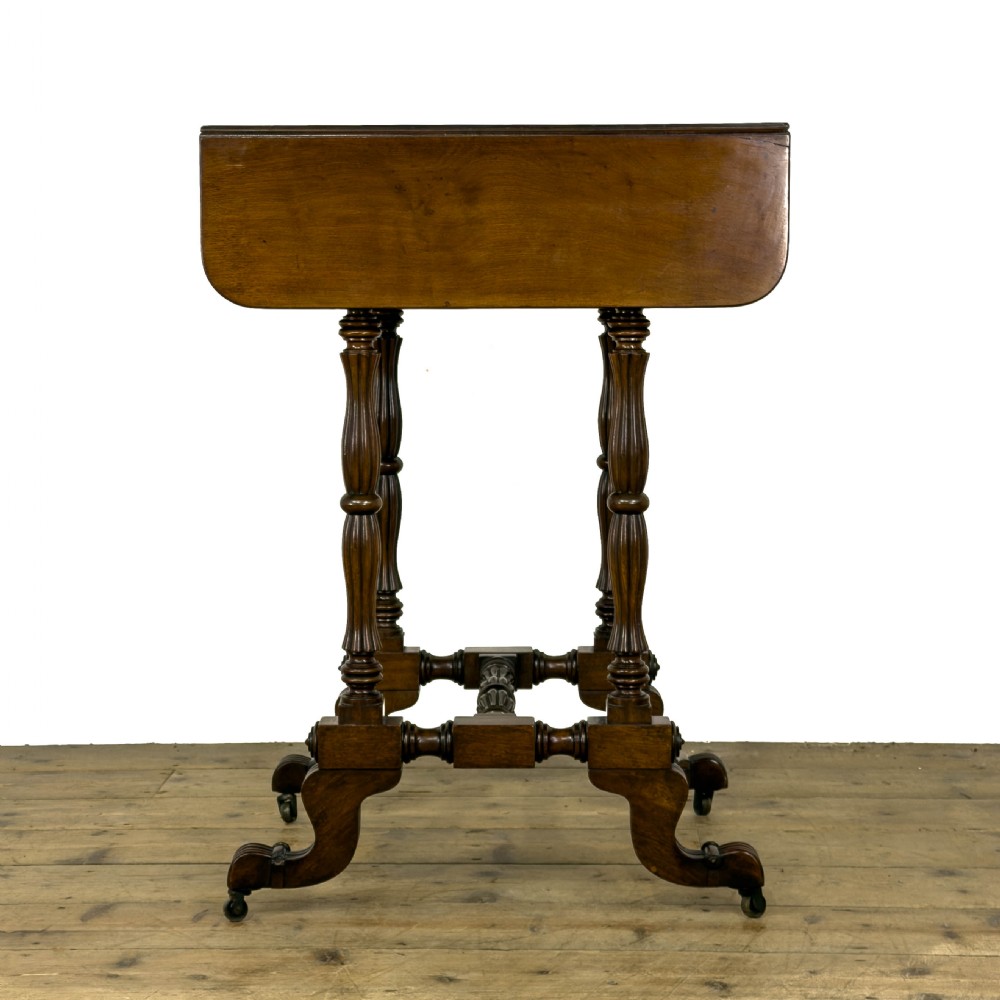 An antique Victorian dark mahogany drop-leaf work table featuring a single drawer with turned wooden knobs, fluted legs, and scroll feet on brass castors. View IV