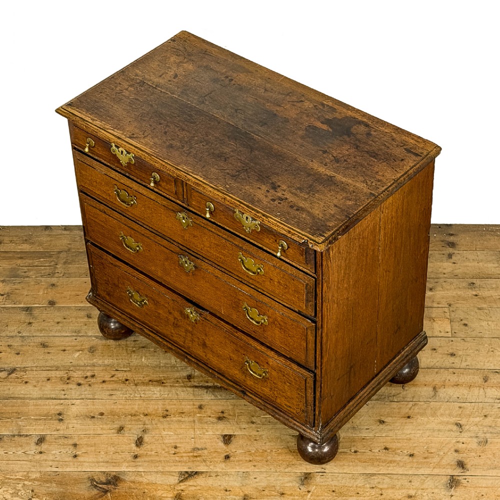 An antique 18th-century oak chest of drawers featuring a two short over three long drawer arrangement, brass handles, and turned bun feet. View III