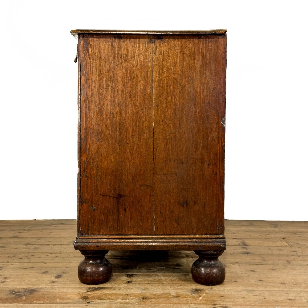 An antique 18th-century oak chest of drawers featuring a two short over three long drawer arrangement, brass handles, and turned bun feet. View IV