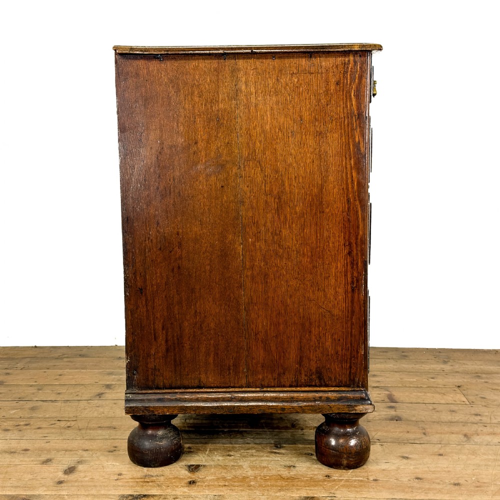 An antique 18th-century oak chest of drawers featuring a two short over three long drawer arrangement, brass handles, and turned bun feet. View VI