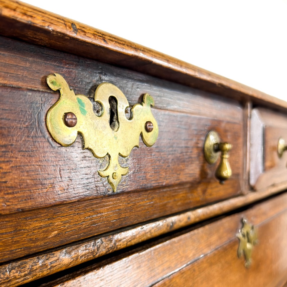 An antique 18th-century oak chest of drawers featuring a two short over three long drawer arrangement, brass handles, and turned bun feet. View XIII