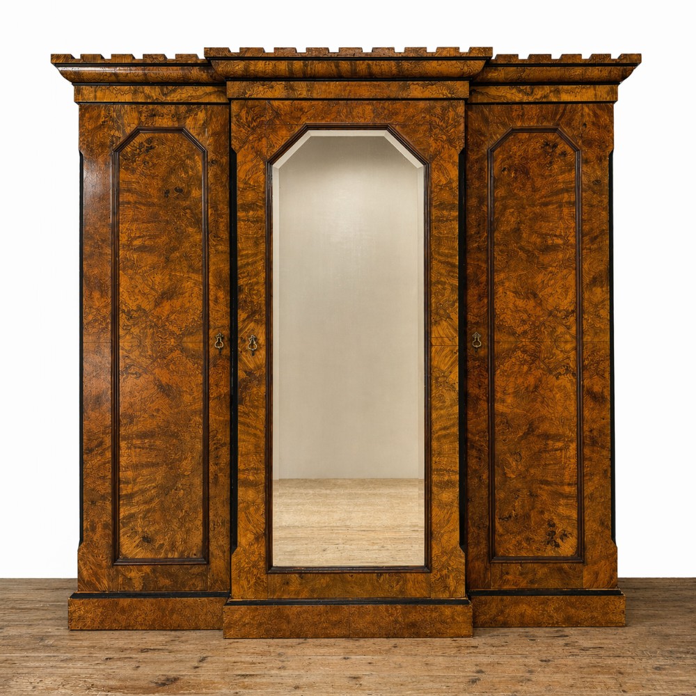 A Victorian burr walnut triple compactum wardrobe with an arched central mirrored door flanked by two panelled timber doors and topped with a castellated cornice.