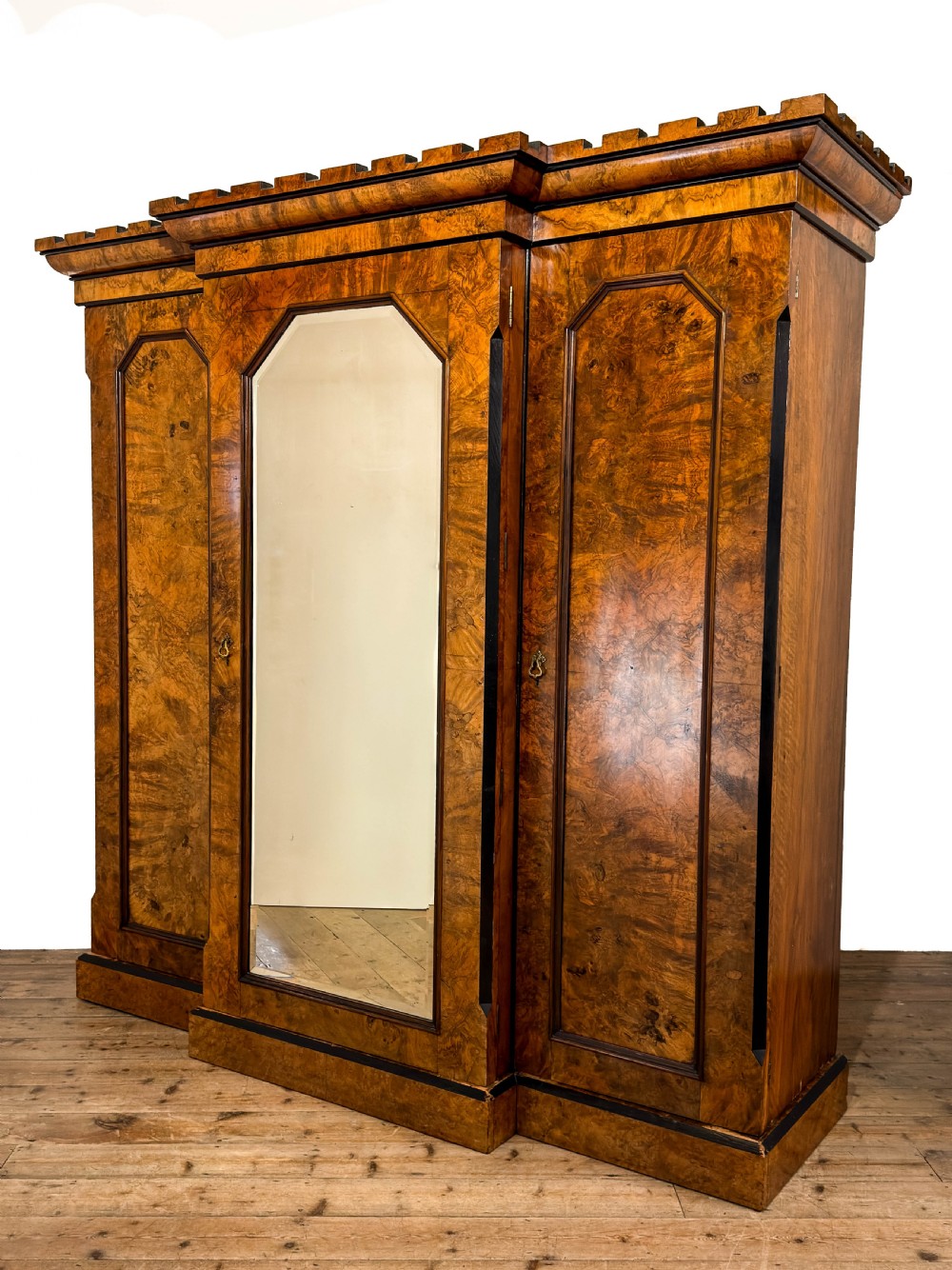 A Victorian burr walnut triple compactum wardrobe with an arched central mirrored door flanked by two panelled timber doors and topped with a castellated cornice. View III