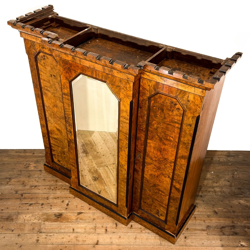 A Victorian burr walnut triple compactum wardrobe with an arched central mirrored door flanked by two panelled timber doors and topped with a castellated cornice. View V