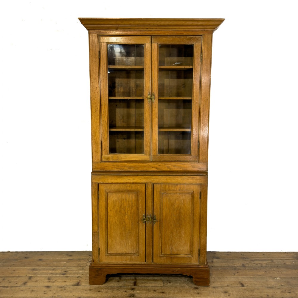 An early 20th-century golden oak cupboard featuring upper glazed double doors over lower solid panelled doors with brass hardware.