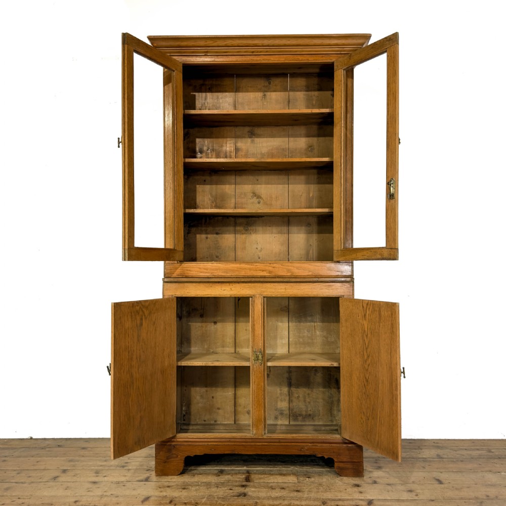 An early 20th-century golden oak cupboard featuring upper glazed double doors over lower solid panelled doors with brass hardware. View IX