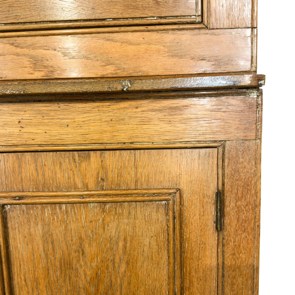 An early 20th-century golden oak cupboard featuring upper glazed double doors over lower solid panelled doors with brass hardware. View X