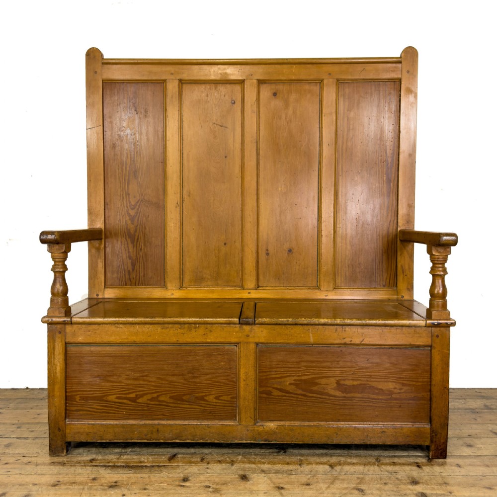 A high-backed antique pine settle bench with a four-panel backrest, turned arm supports, and a hinged seat box.