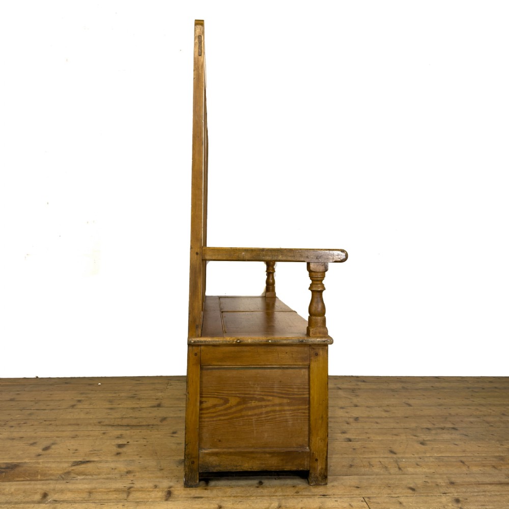A high-backed antique pine settle bench with a four-panel backrest, turned arm supports, and a hinged seat box. View V