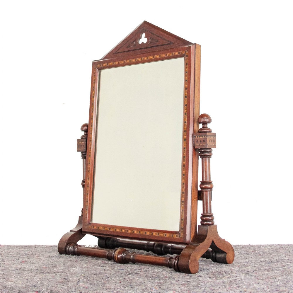 A Victorian Gothic mahogany swing mirror featuring a pointed arch pediment with a trefoil cutout, turned side columns, and geometric inlay borders.