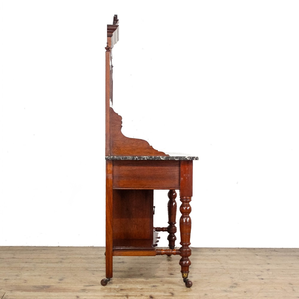 An Edwardian mahogany washstand featuring a tiled splashback with a central mirror, a grey marble top surface, two drawers, a lower cupboard, and turned legs on castors. View IV