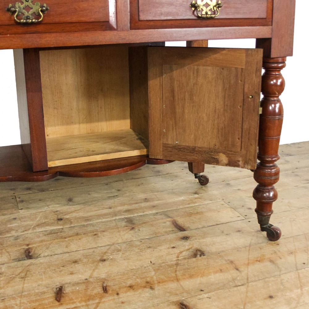An Edwardian mahogany washstand featuring a tiled splashback with a central mirror, a grey marble top surface, two drawers, a lower cupboard, and turned legs on castors. View IX