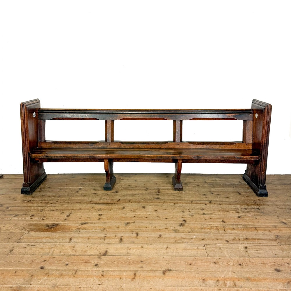 A long 19th-century oak church pew featuring carved Gothic tracery on its end panel and an open frame back. View II
