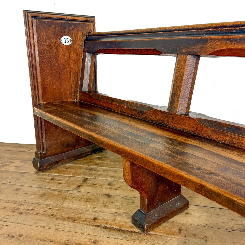 A long 19th-century oak church pew featuring carved Gothic tracery on its end panel and an open frame back. View VI
