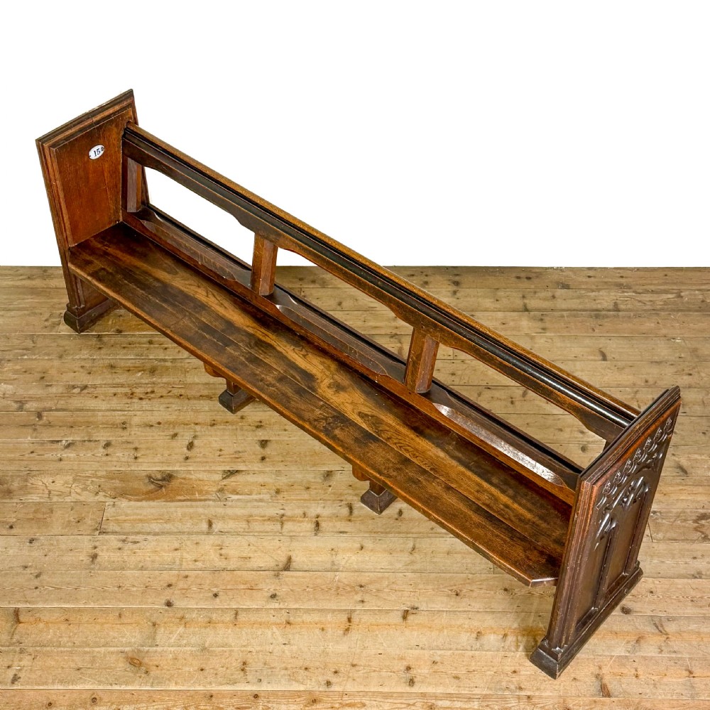 A long 19th-century oak church pew featuring carved Gothic tracery on its end panel and an open frame back. View VII