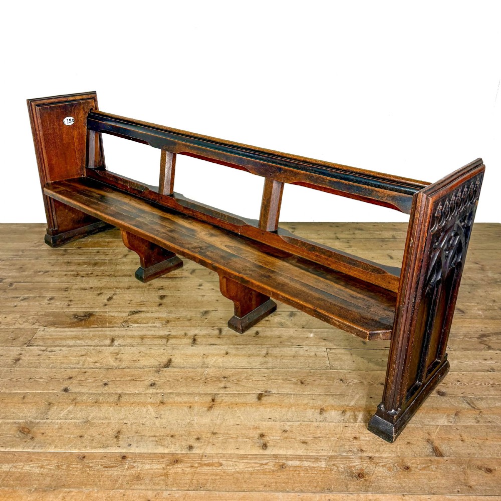 A long 19th-century oak church pew featuring carved Gothic tracery on its end panel and an open frame back. View VIII