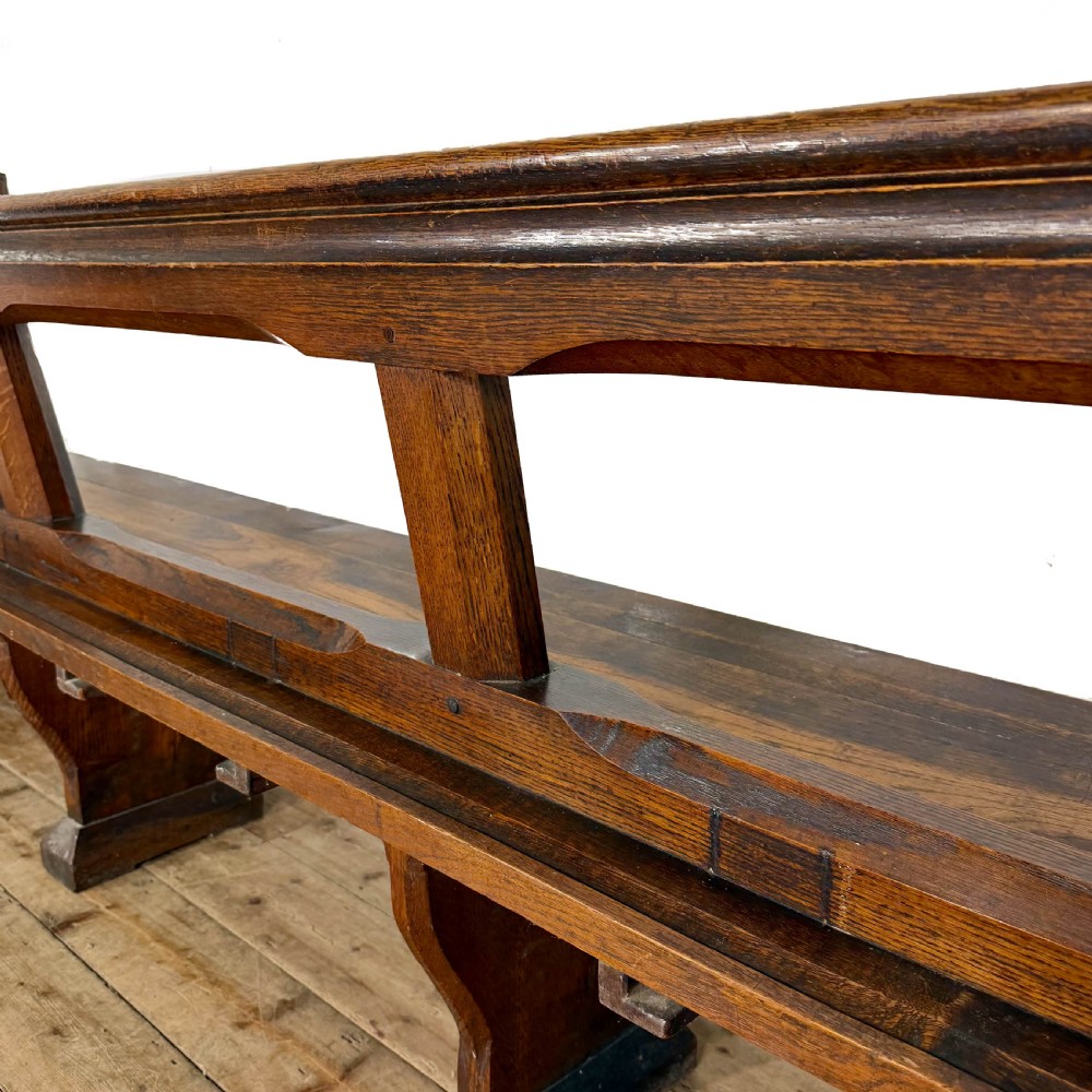 A long 19th-century oak church pew featuring carved Gothic tracery on its end panel and an open frame back. View X