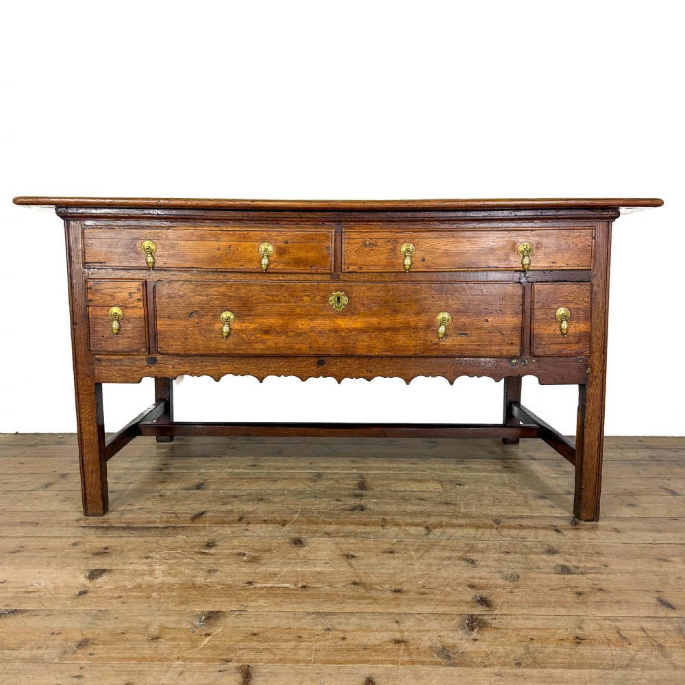 An antique oak serving table featuring brass drop handles, multiple drawer compartments, a scalloped apron, and straight legs connected by stretchers.